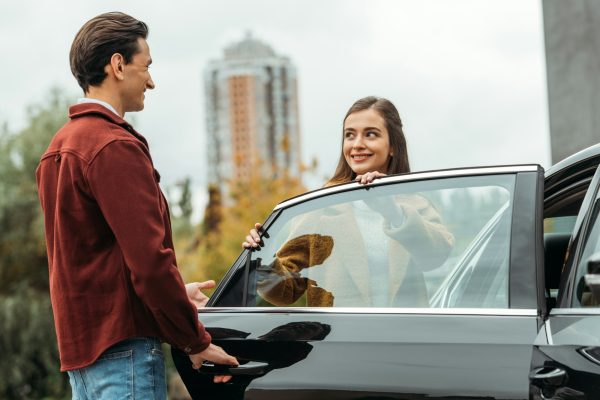 Smiling taxi driver opening car door for woman